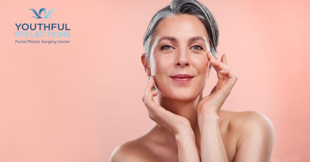 Woman in her 60's smiling and framing her face with her hands (model).